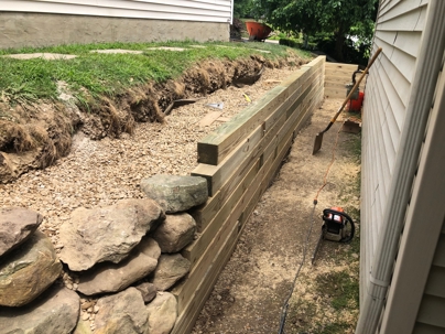 A newly built timber retaining wall separates a house from a gravel-filled trench with large rocks.