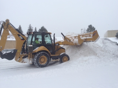 A yellow CAT backhoe loader clears snow from a paved area.