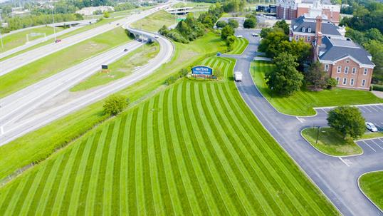 Aerial view of a campus entrance with a striped lawn leading to university buildings. A sign displays 'WILMINGTON UNIVERSITY' next to a highway.