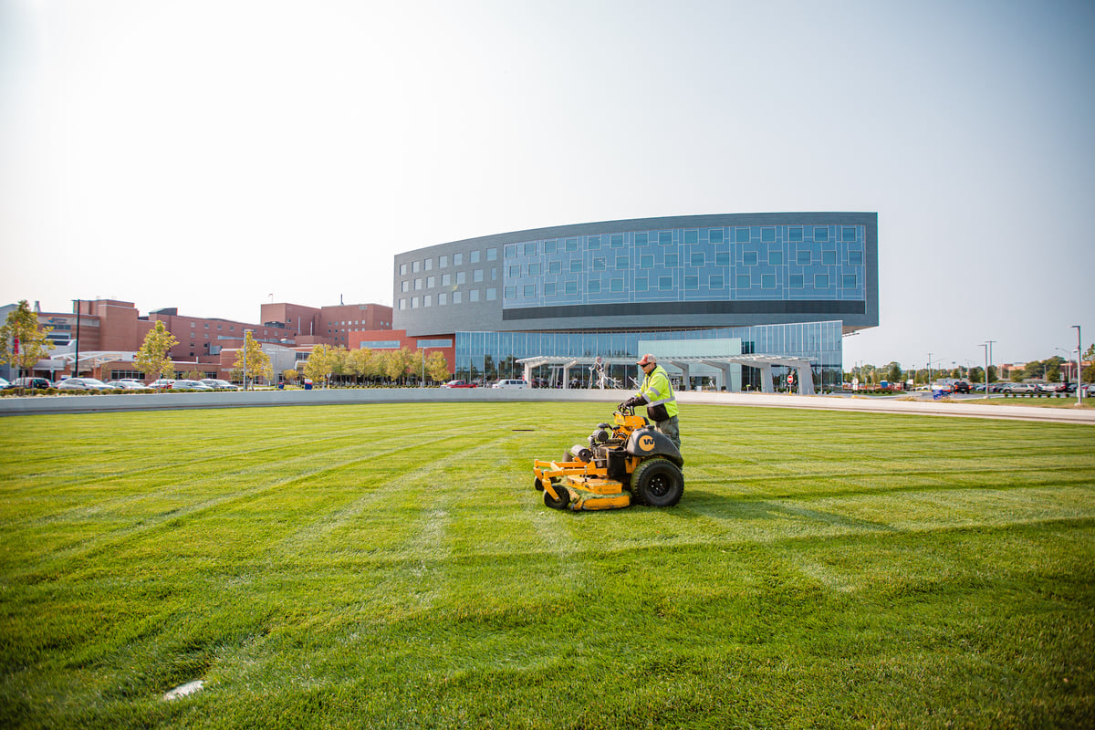 landscape maintenance team mowing large grass area in front of commercial building