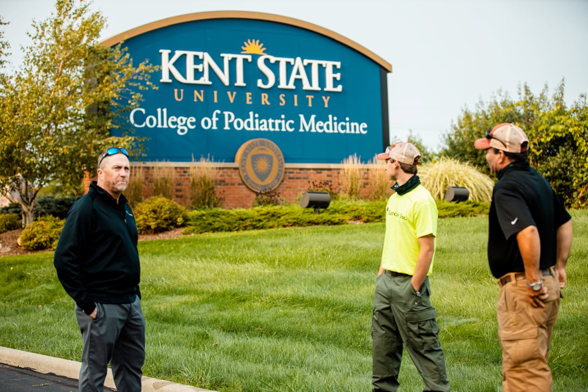 large sign at Kent State with neat landscaping and team meeting 