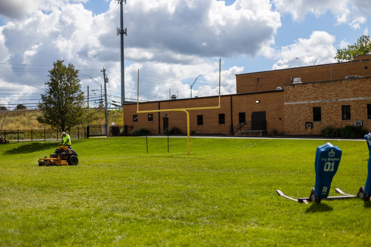 landscape maintenance team mows lawn on football field at school