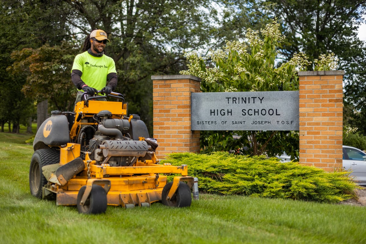 commercial landscape maintenance team member mows lawn at high school