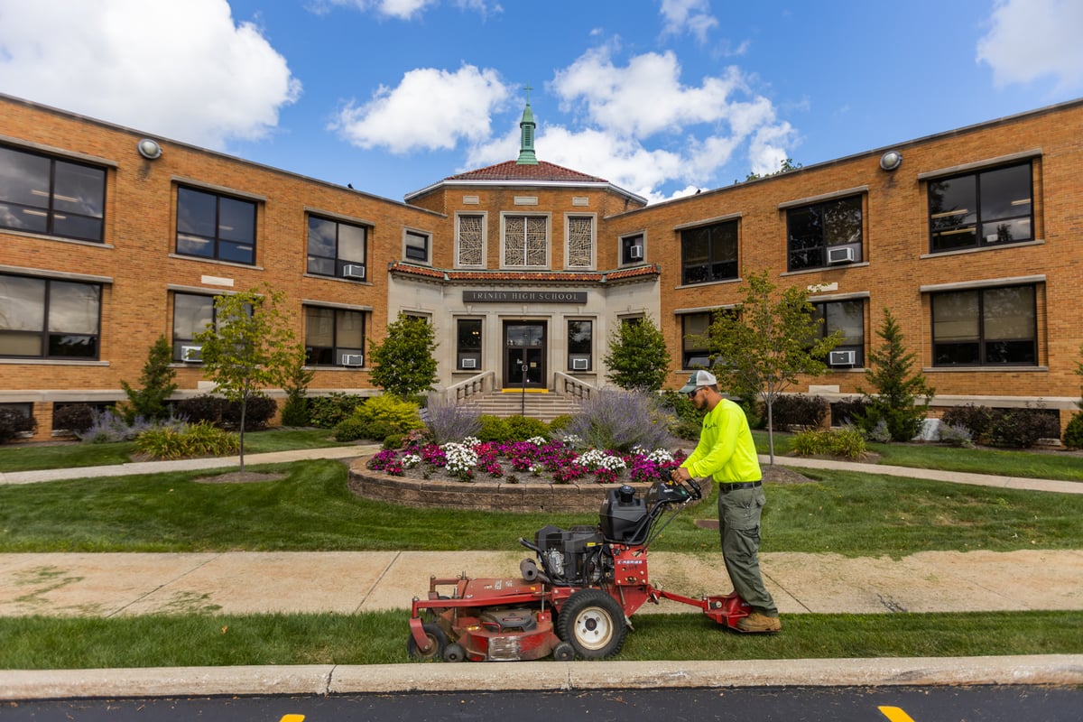 commercial landscape maintenance team mows lawn in front of high school