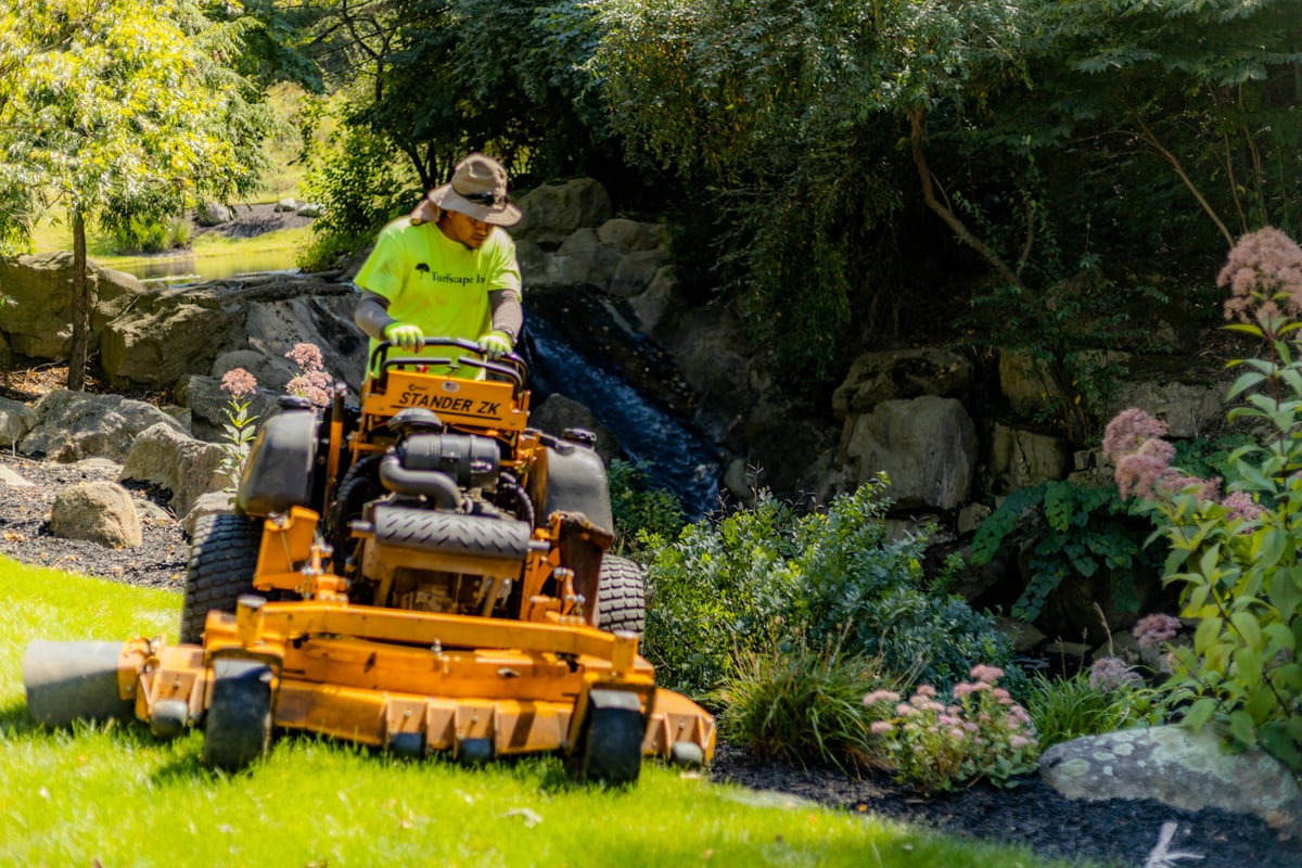 landscape maintenance team mows lawn with water feature in background