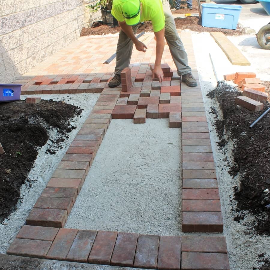 landscape installation professional lays pavers for walkway