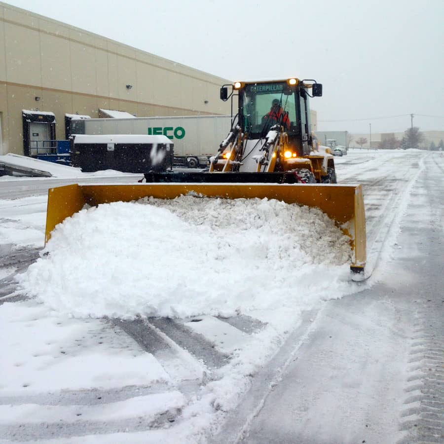plow removing snow from commercial property with lights on
